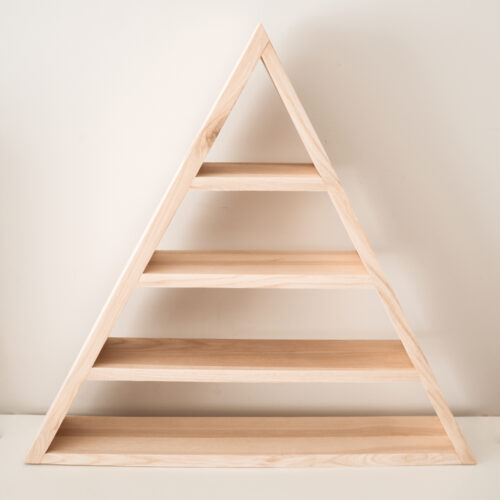 Zdjęcie produktowe przedstawiającą półkę - model triangle - czyli półkę trójkątną. Półka ze zdjęcia jest wykonana z drewna, jest to lity jesion w jasnym odcieniu. Półka ma trójkątny kształt, i trzy piętra (cztery, jeśli liczyć również dolną podstawę).